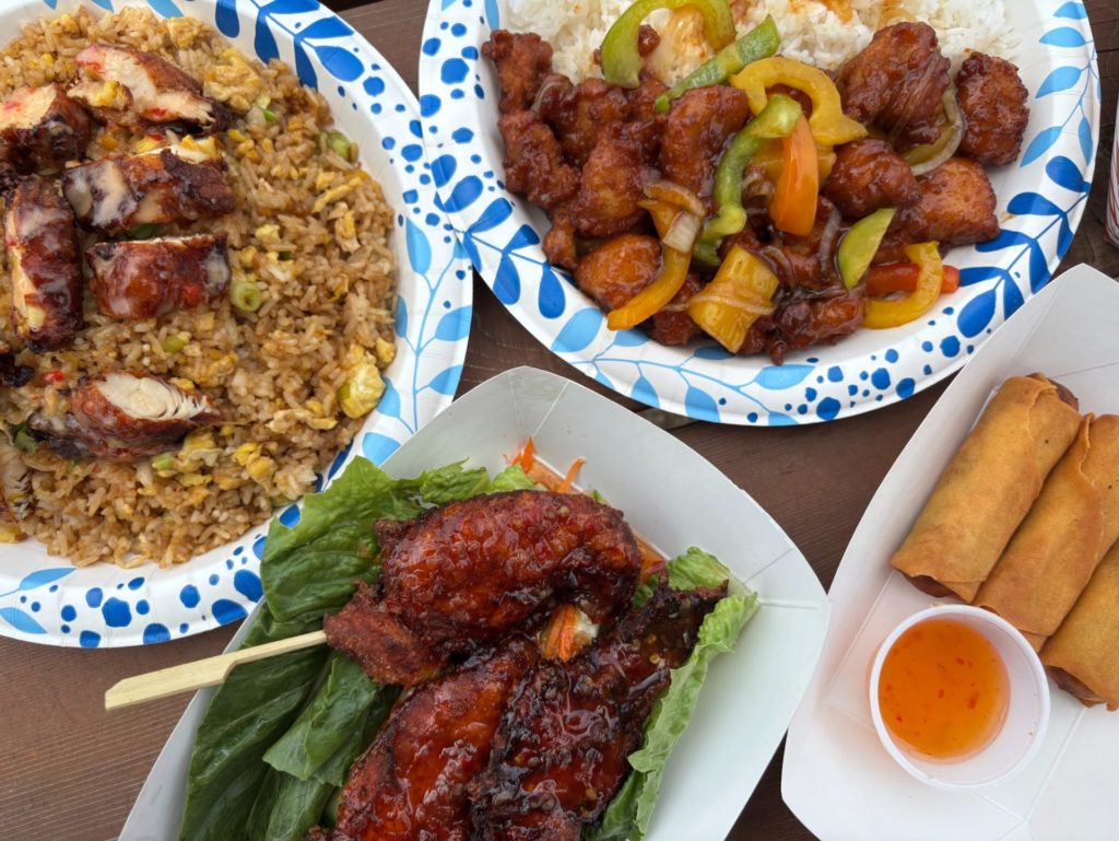 A spread of Lucky Eddy's dishes: fried rice, pineapple chicken, satay, and egg rolls