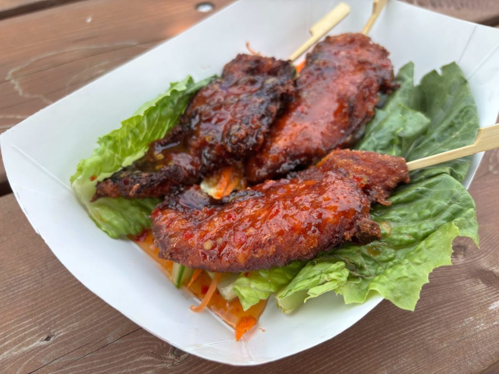 Glazed chicken satay skewers over lettuce in a paper tray
